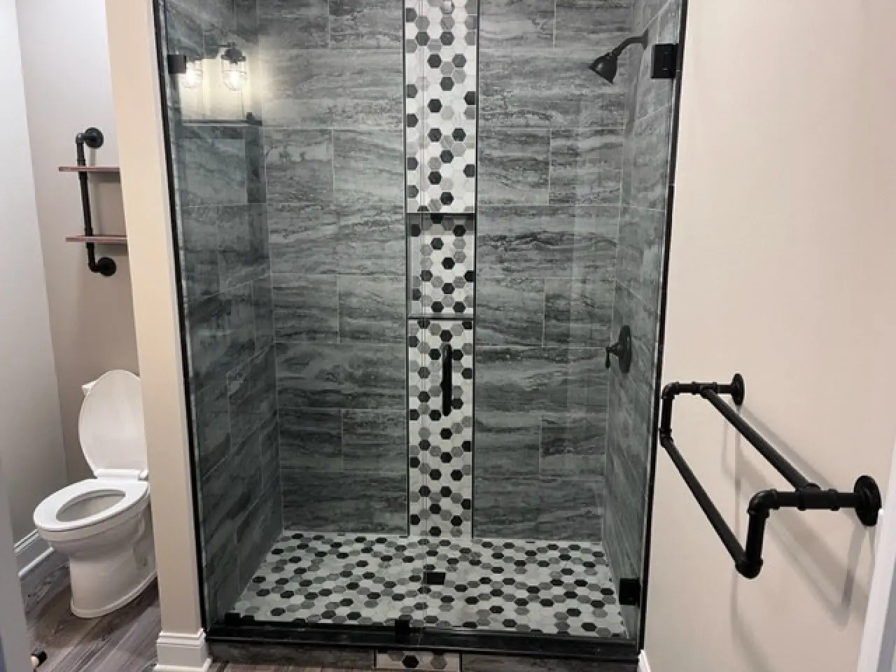 A modern bathroom featuring a glass shower with black and white polka dot tiles, and a toilet in the background.