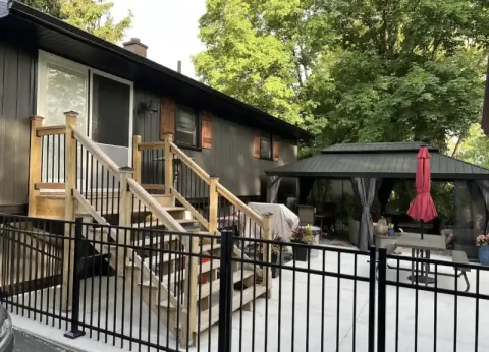 A fenced backyard with a patio, gazebo, stairs, potted plants, and outdoor furniture.