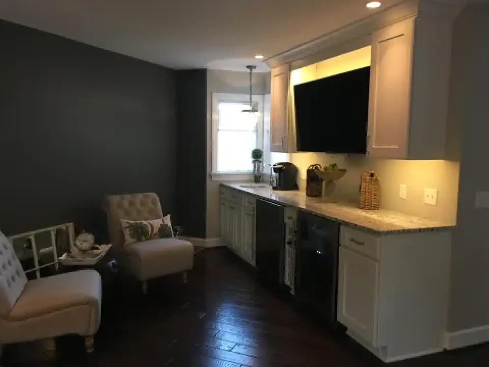 Cozy kitchenette with white cabinets, dark accent wall, two chairs, and window lighting.