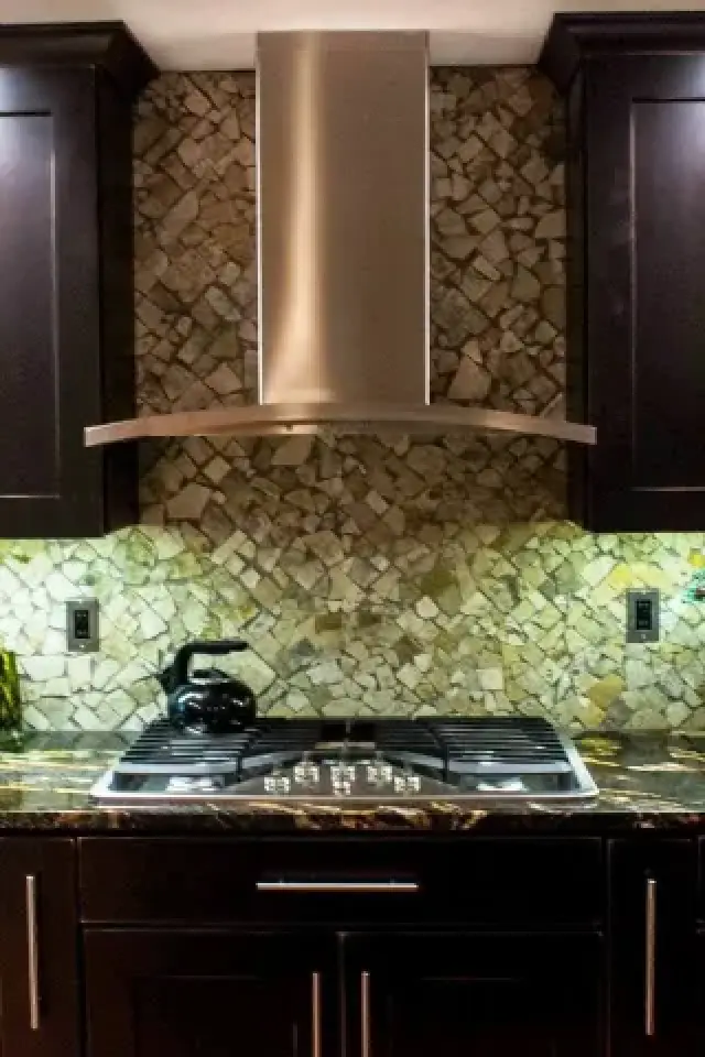 Stove with a steel range hood, mosaic tile backsplash, and dark cabinets in a kitchen.