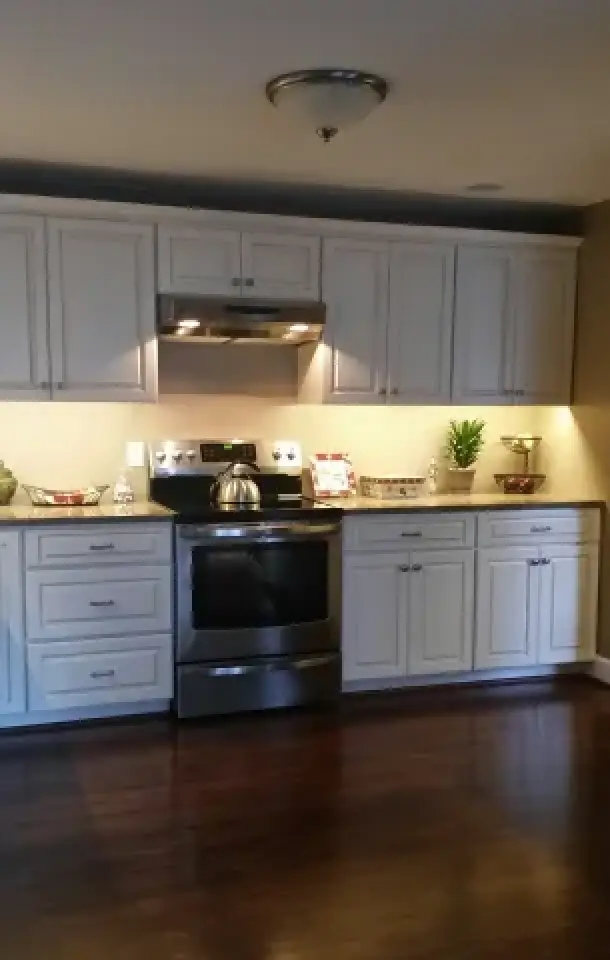 Modern kitchen with white cabinets, stainless steel stove, and dark wooden floors.