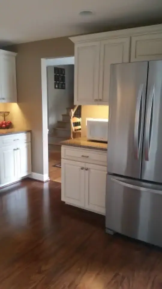 Modern kitchen with white cabinets, stainless steel fridge, and wooden floor near a staircase.