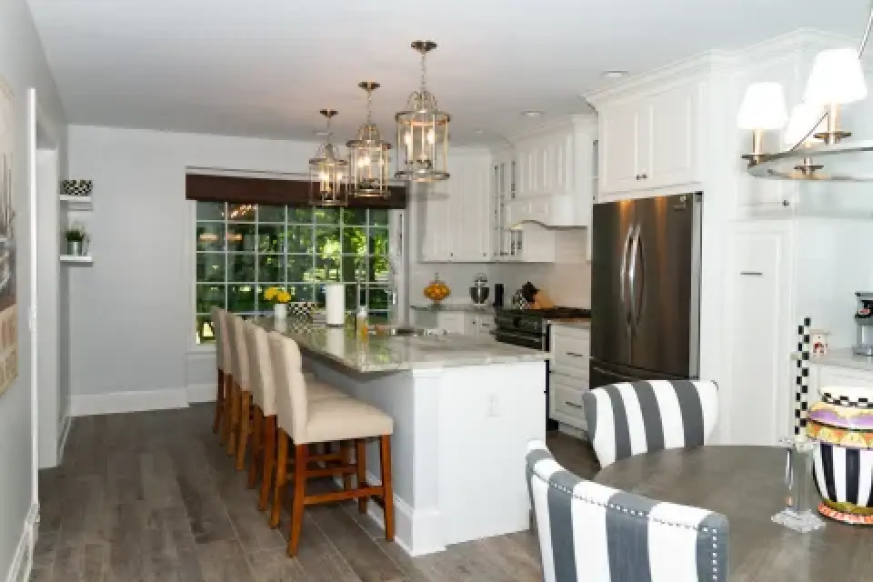 Modern kitchen with white cabinets, island seating, pendant lights, and a round dining table.