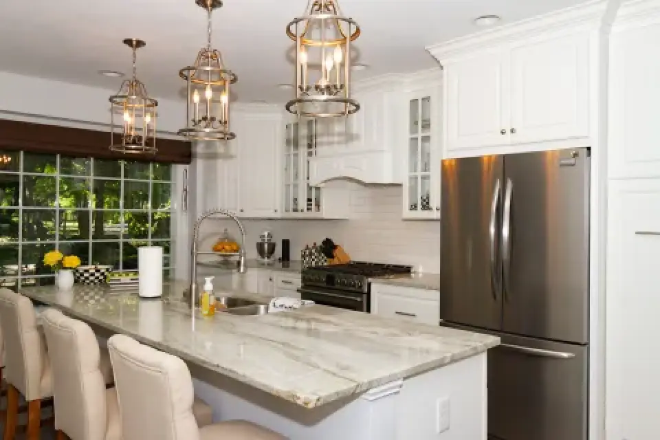 Modern white kitchen with marble island, stainless steel appliances, and pendant lights.