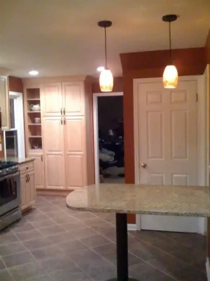 Modern kitchen with pendant lights, granite island, tile floor, and light wood cabinets.