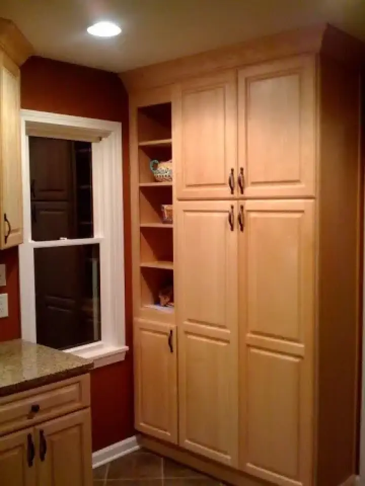 Tall light wood kitchen cabinets with shelves beside a window and dark red walls.
