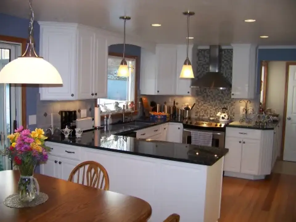 Modern kitchen with white cabinets, black countertops, wood floor, and a dining table with flowers.