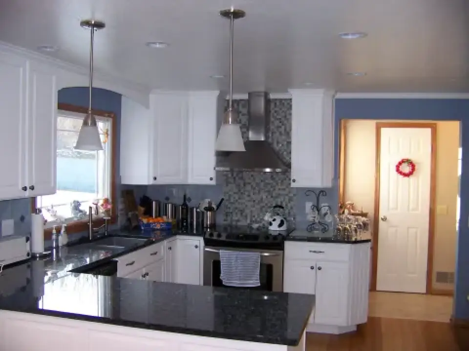 Modern kitchen with white cabinets, black countertops, and stainless steel appliances.