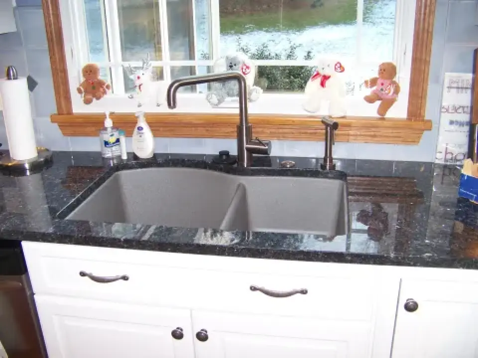 A kitchen sink with a black faucet, soap dispensers, and plush toys on the window ledge.