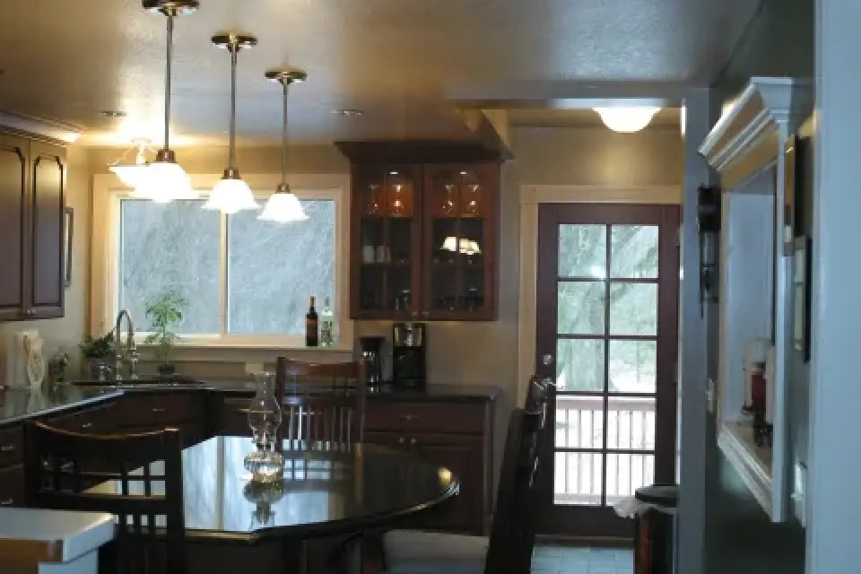 Modern kitchen with dark cabinets, a glass table, pendant lights, and a door to the outside.