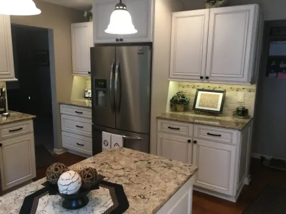 Modern kitchen with stainless steel fridge, white cabinets, and a decorated granite island.