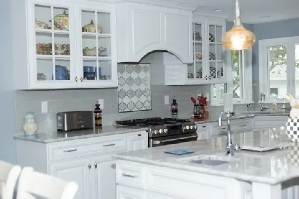 Bright, modern kitchen with white cabinets, marble countertops, and glass-front upper doors.