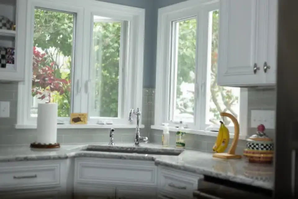 Bright kitchen with white cabinets, granite countertops, and large windows overlooking greenery.