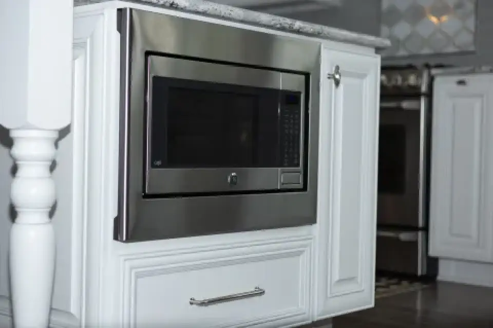 Built-in stainless steel microwave installed in white kitchen cabinetry above a cabinet drawer.