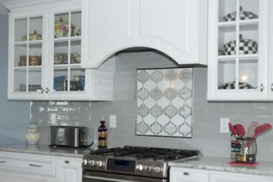 A kitchen with white cabinets, a gas stove, and glass-front cupboards displaying dishes.
