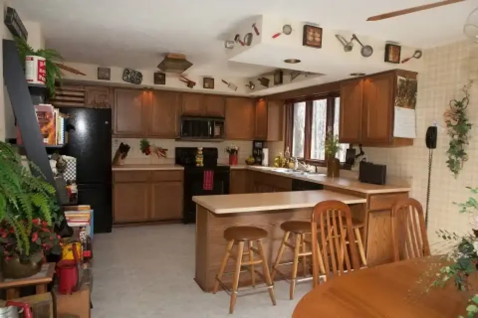 A kitchen with wooden cabinets, black appliances, and utensils as decorations near the ceiling.