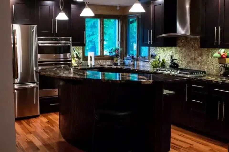 Modern kitchen with dark cabinets, stainless steel appliances, and a granite island countertop.