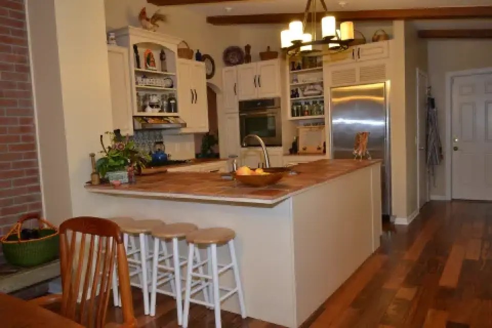 A kitchen with a central island, three stools, stainless appliances, and wooden floors.