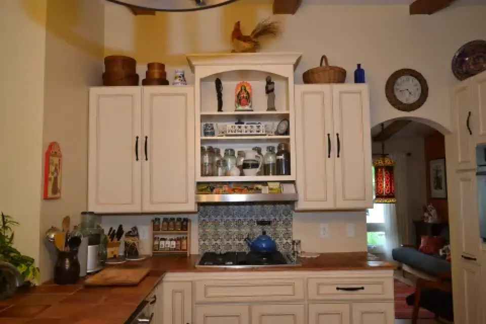A cozy kitchen with cream cabinets, spice jars, and decorative items on the shelves and countertops.