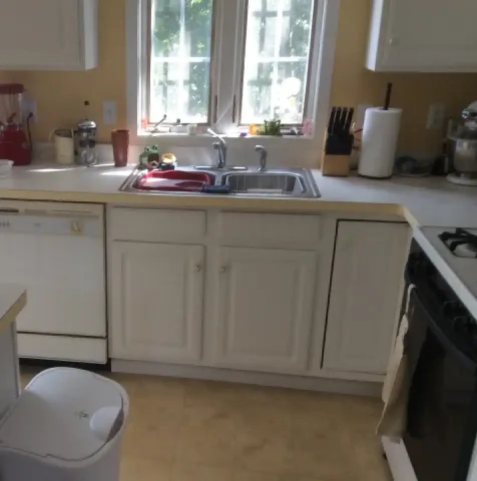 White kitchen with a sink under a window, dishwasher, and countertop appliances visible.