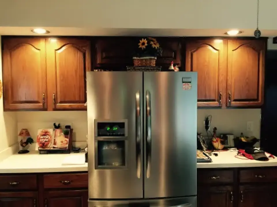 A stainless steel fridge in a kitchen with wooden cabinets and various items on the counters.