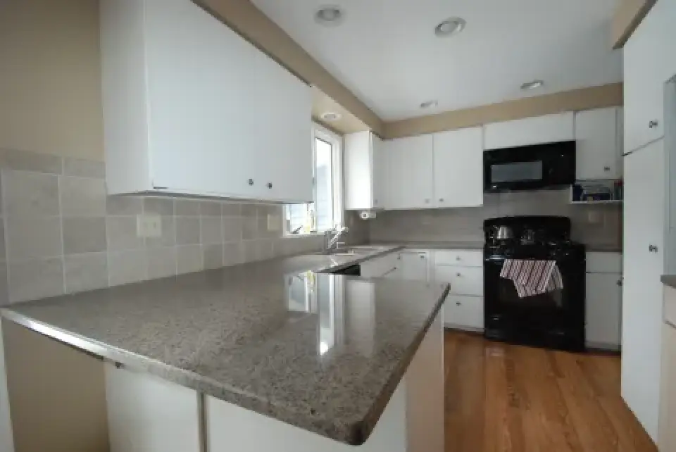 Modern kitchen with white cabinets, granite countertops, black appliances, and wood flooring.