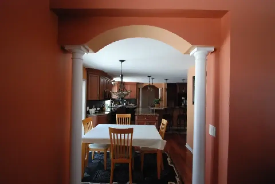 A dining table with four chairs is set under an archway, leading into a kitchen area.