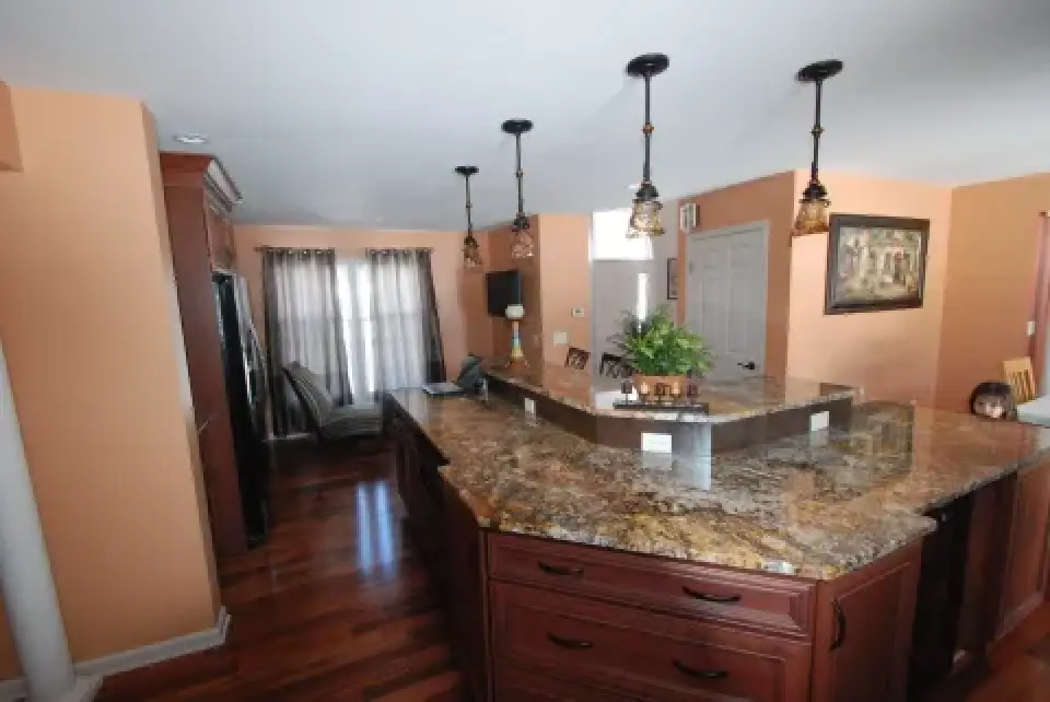 Kitchen with granite countertops, pendant lights, wood floors, and peach-colored walls.
