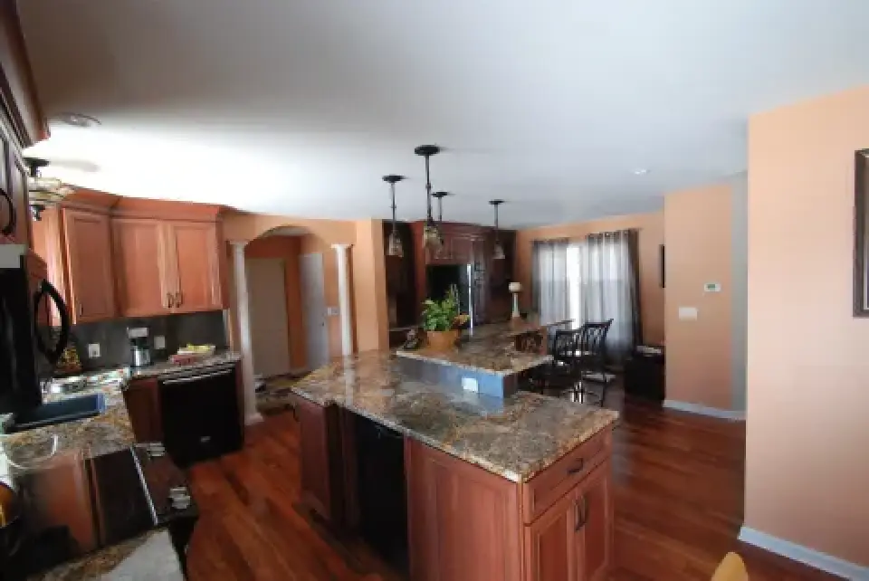 Spacious kitchen with wooden cabinets, granite countertops, and a dining area in the background.