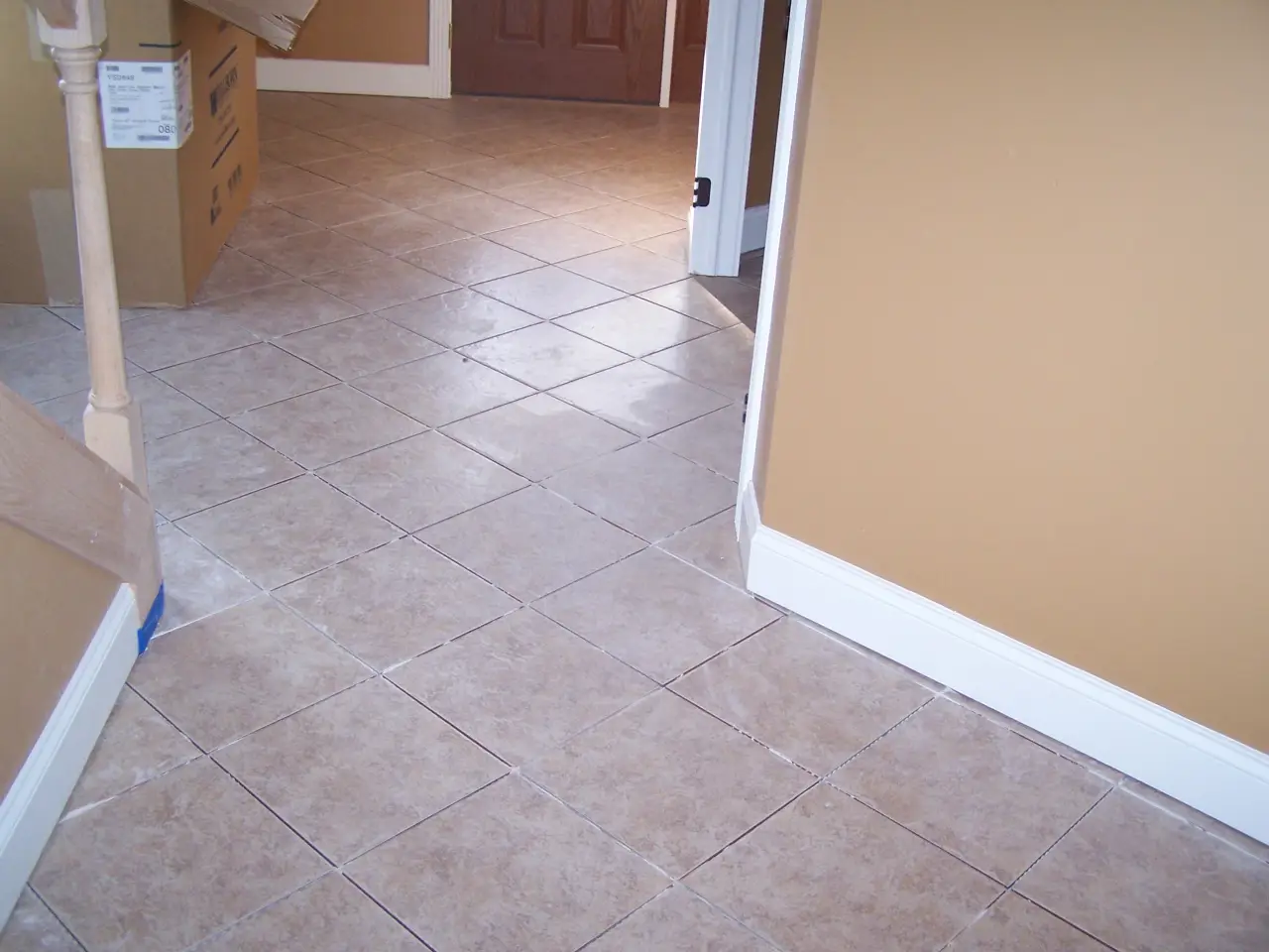 A tiled floor with light brown tiles, leading to a doorway. Walls are painted in a warm beige color. Boxes are visible in the background.