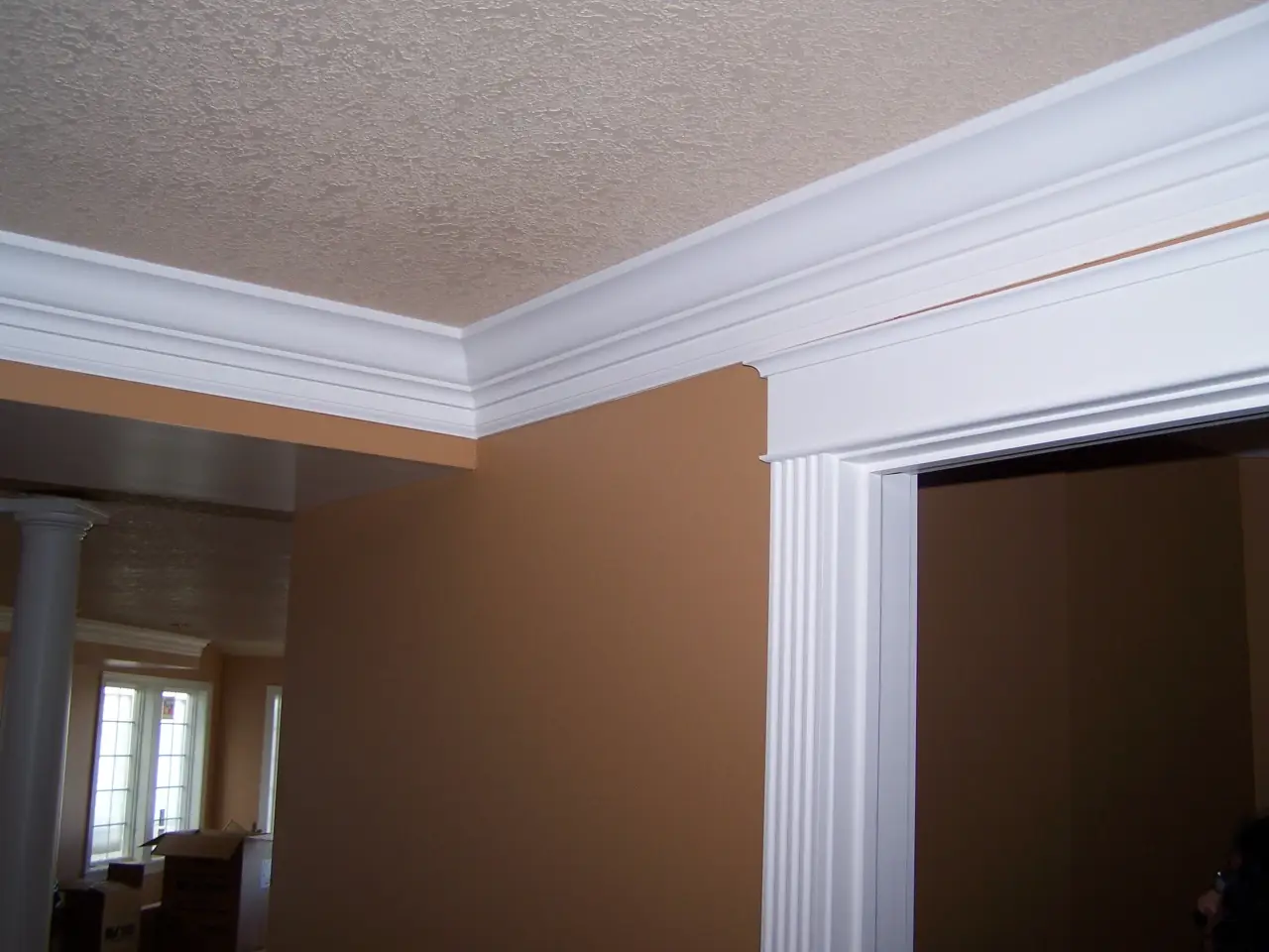 Interior corner of a room featuring white crown molding and trim against a beige wall.