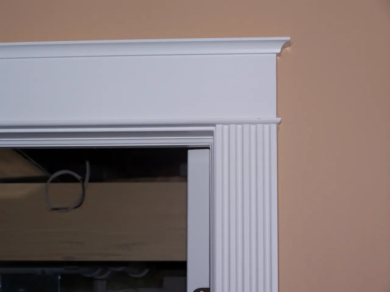 Close-up of a white door frame with decorative molding against a beige wall.