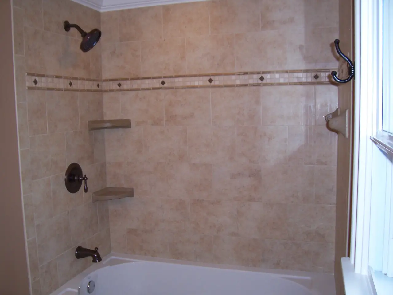A bathroom with a tiled shower area, featuring a bathtub, showerhead, and two shelves. The walls are light-colored with decorative trim.