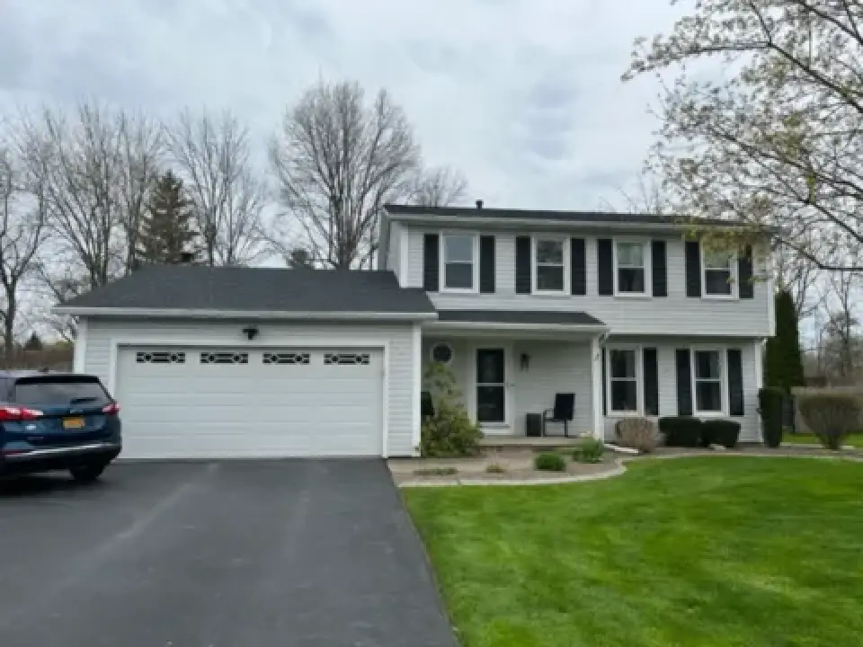 Two-story white house with black shutters, attached garage, driveway, and green lawn.