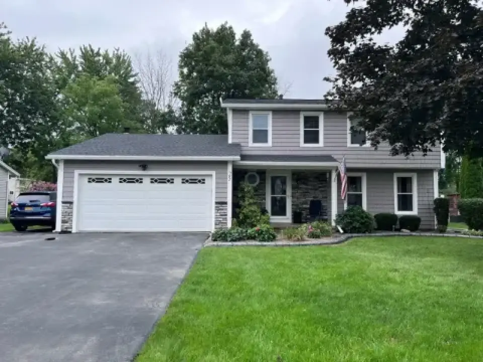 Two-story suburban house with gray siding, a white garage, and a well-kept front lawn.