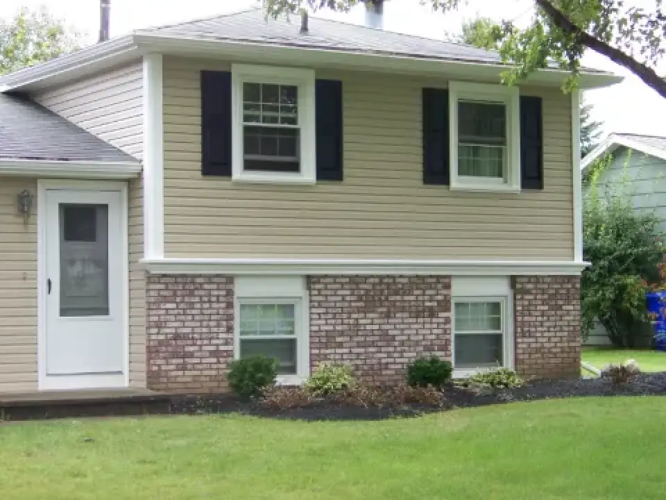 Two-story house with beige siding, brick lower level, black shutters, and a white door.