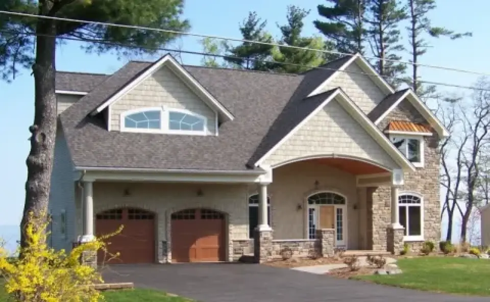 Two-story suburban house with stone and shingle exterior, double garage, and landscaped yard.