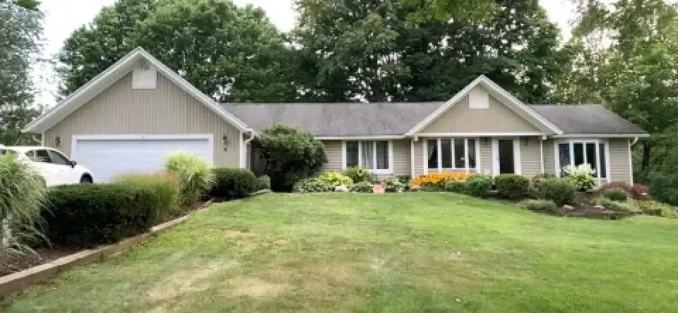 Single-story beige house with white trim, a two-car garage, and a well-kept lawn and garden.
