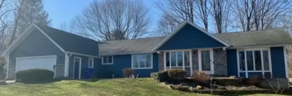 Single-story blue house with stone accents, attached garage, and bare trees in the background.