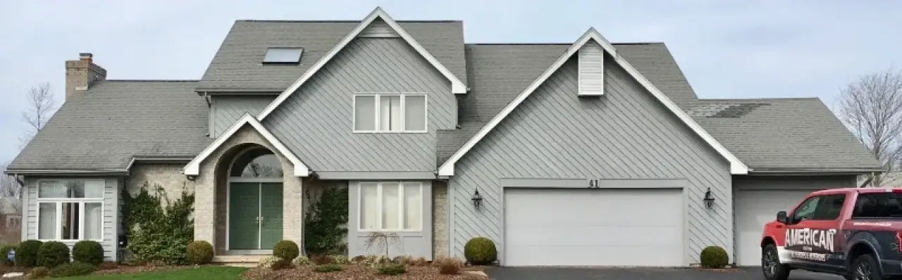 Gray two-story house with a double garage, green lawn, and red utility truck parked outside.