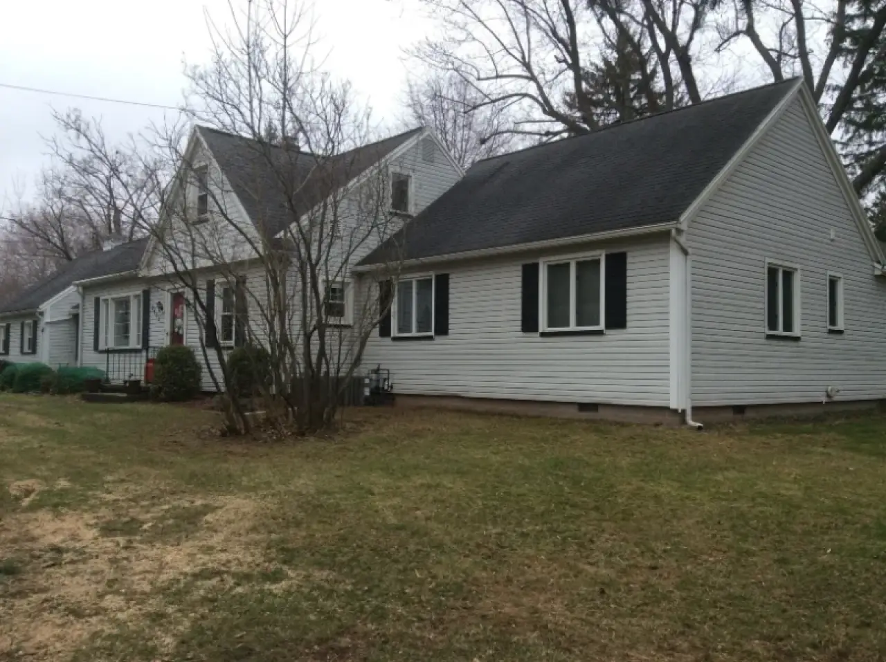 White single-story house with black shutters, gable roof, bare trees, and a patchy lawn.