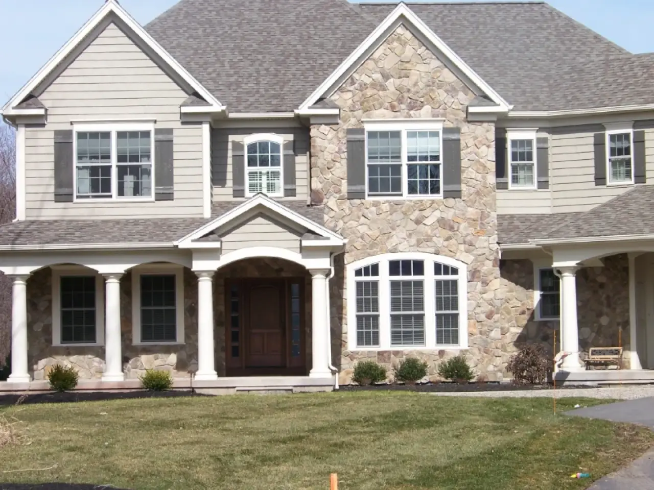 Two-story house with stone and siding exterior, columns, and a manicured front lawn.