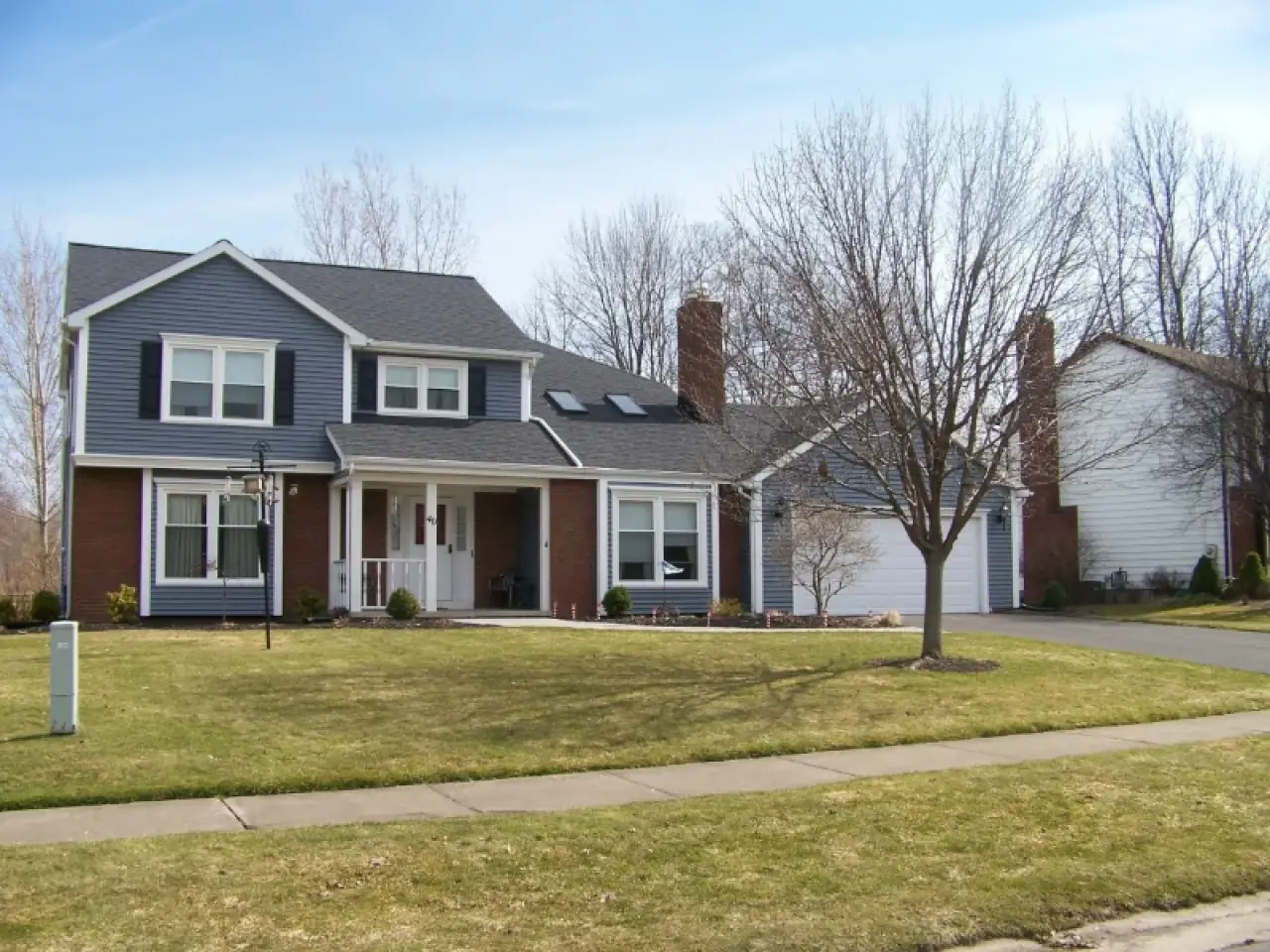 Two-story suburban house with gray siding, brick accents, and a leafless tree in the front yard.