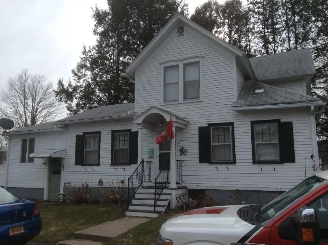 White two-story house with black shutters and front steps, a red flag hangs by the door.