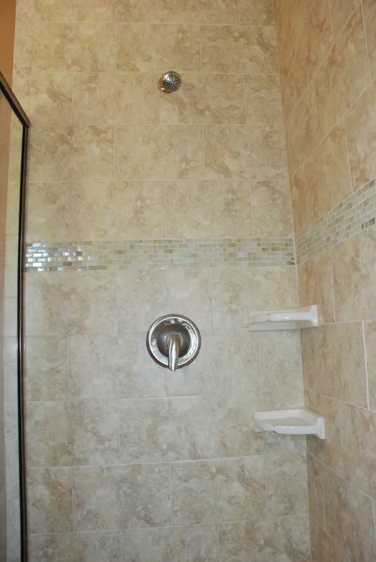 A modern shower with tiled walls, a chrome faucet, and two white shelves for toiletries.