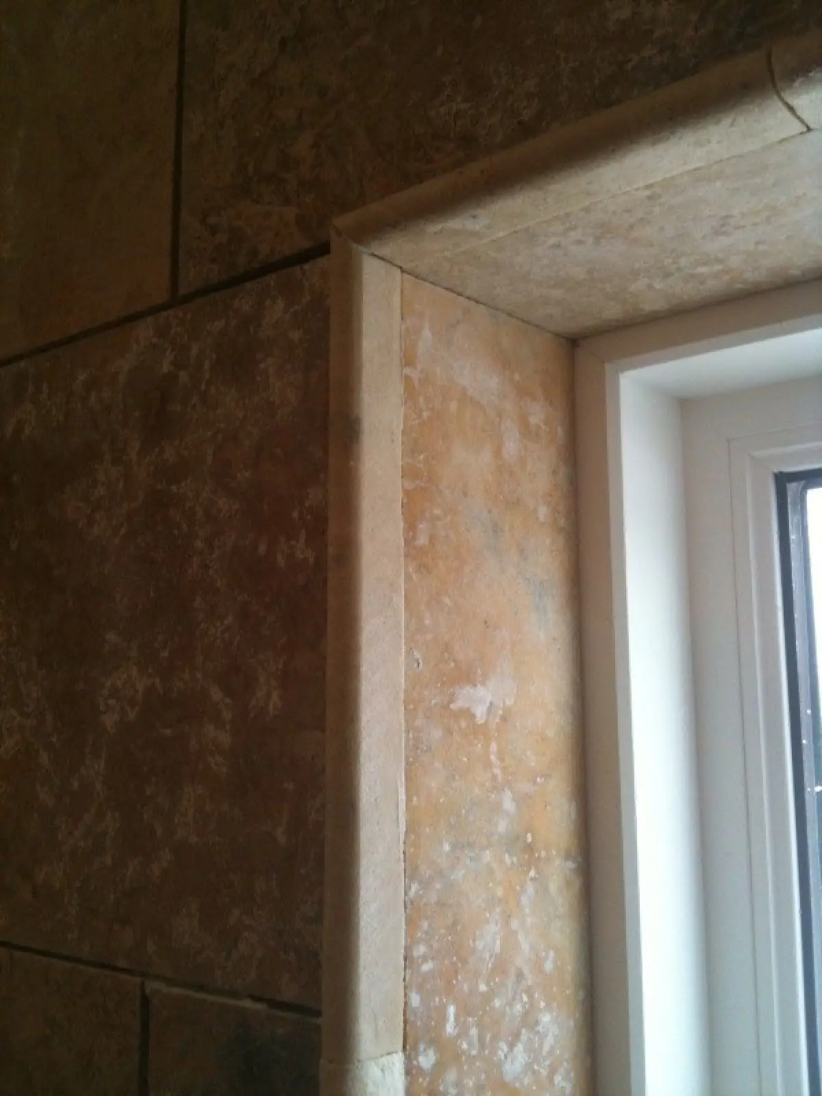 Close-up of a wall corner featuring textured stone tiles and a window frame.