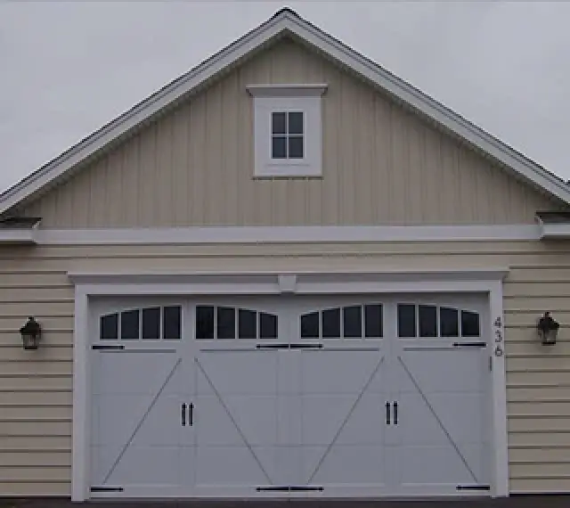 Beige house with white double garage doors, black handles, and a small window above the garage.