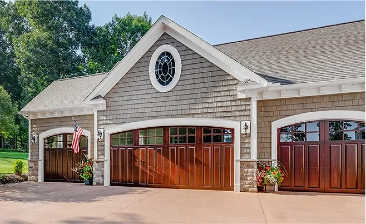 Three-car garage with wooden doors, shingle siding, stone accents, and an American flag.