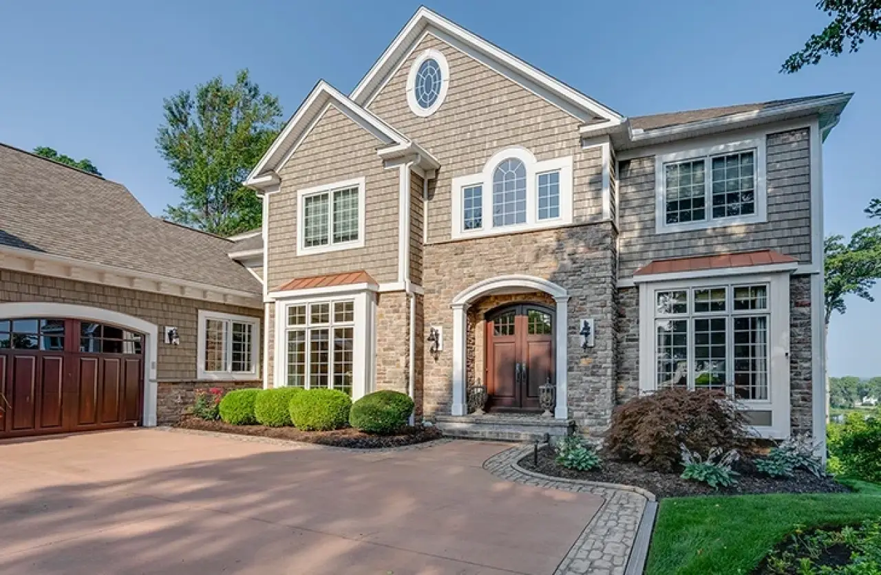 Two-story suburban house with stone and shingle exterior, large windows, and landscaped yard.
