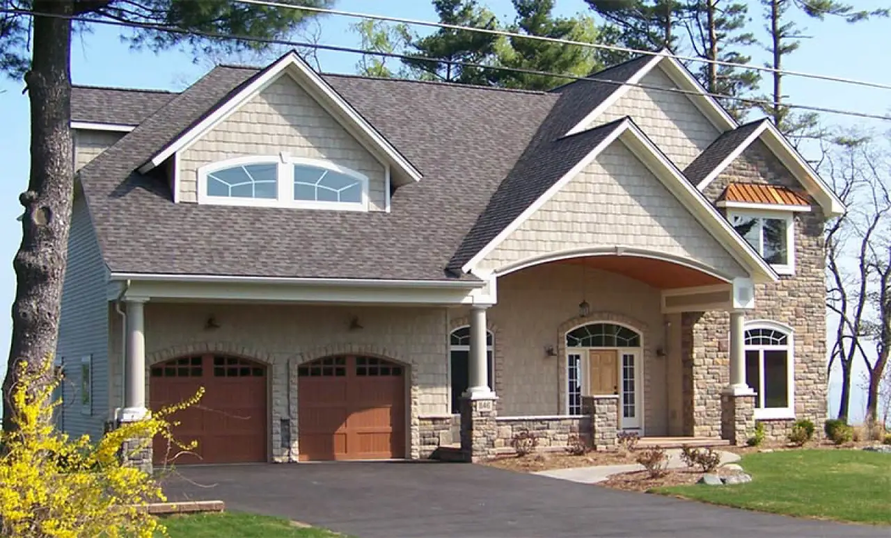 Two-story suburban house with stone and shingle exterior, double garage, and arched entryway.